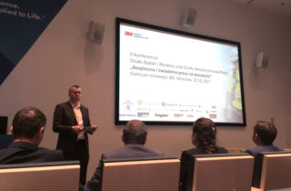 Prelegent przedstawia gości II Konferencji Działu Badań i Rozwoju 3M „Bezpieczna i świadoma praca na wysokości”. W tle ekran prezentujący tematykę konferencji.