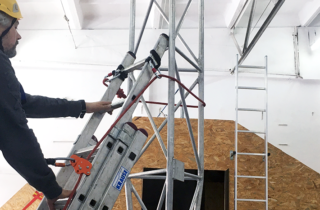 mężczyzna w kasku wchodzący po drabinie z zastosowaniem giętkiej prowadnicy EN 353-2